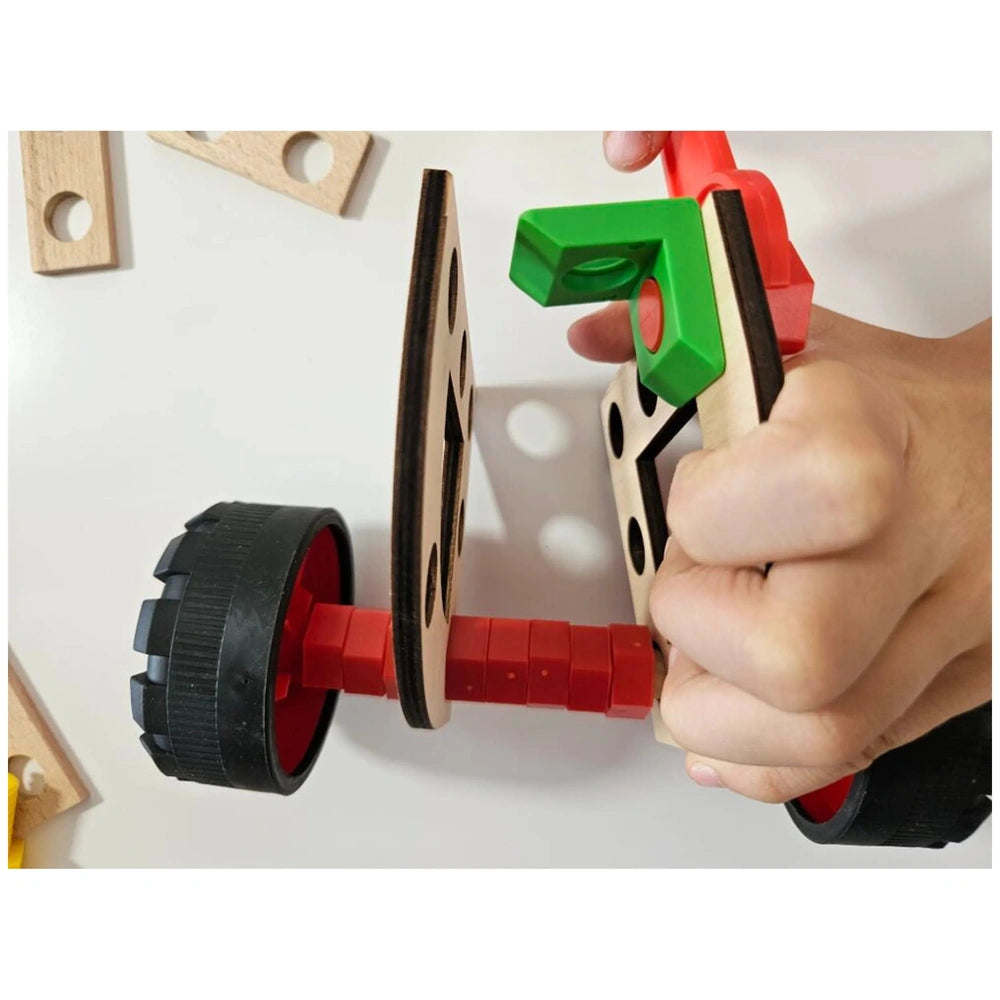 Child assembling Alexander Maly Constructor Junior toy with red wheels, wooden pieces, and green connector.