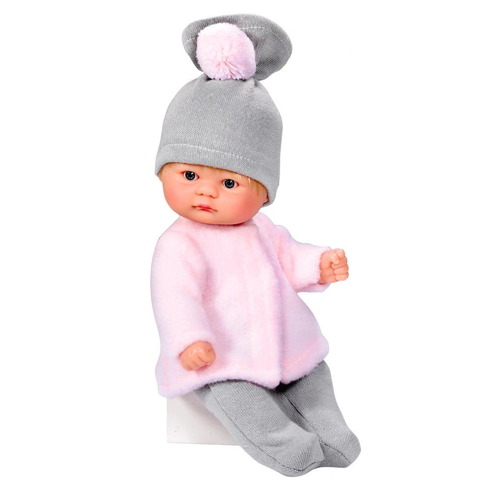 Asi Dolls Bomboncin in a pink coat and grey hat with pom-pom, sitting and looking forward.