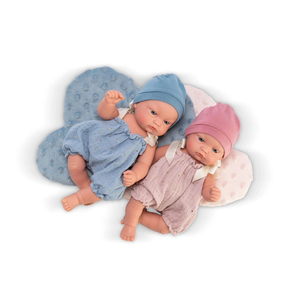 Two ASI dolls lie on blue and pink cloud cushions, wearing matching blue and pink rompers and hats.