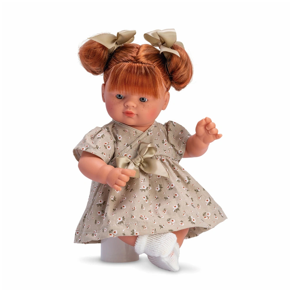 Red-haired doll with pigtails, wearing a green flower dress and bows, posed sitting with bent arm and white socks.