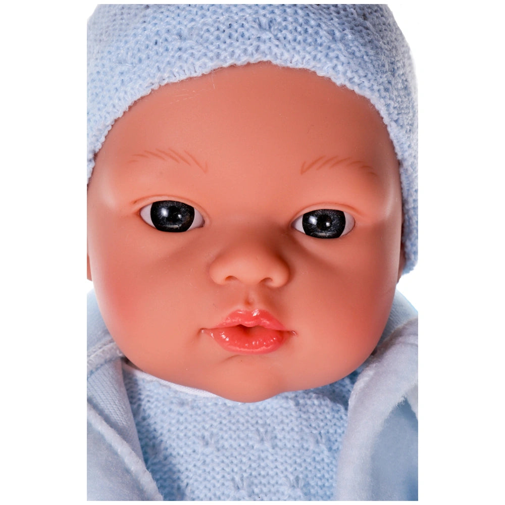 Lifelike Koke doll with blue eyes and knitted blue hat, showcasing realistic features and rosy cheeks.