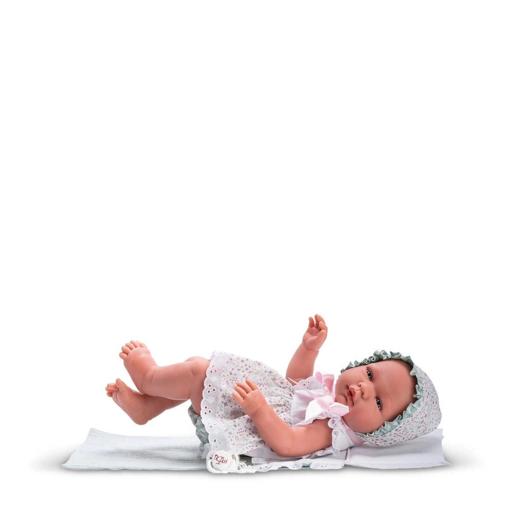 Asi Doll María in a floral Cloe Collection dress and bonnet, lying on a white blanket.