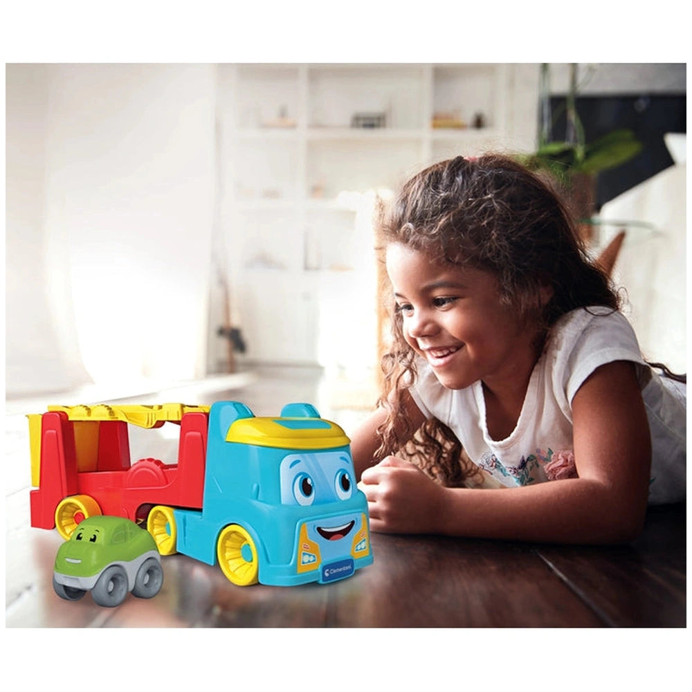 Baby Clementoni 2 In 1 Tumbling Cars Transporter toy truck in blue, yellow, and red beside a smiling girl in a white shirt.