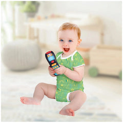 Baby Telecomando toy cell phone held by a smiling child in a green outfit, sitting on a light-colored indoor floor.