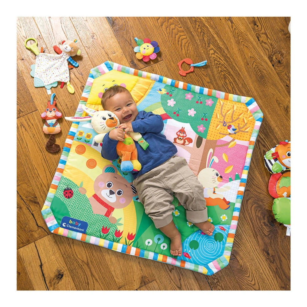 Baby Clementoni Benny The Puppy stuffed animal is held by a smiling baby on a colorful plush mat, enhancing a joyful playtime