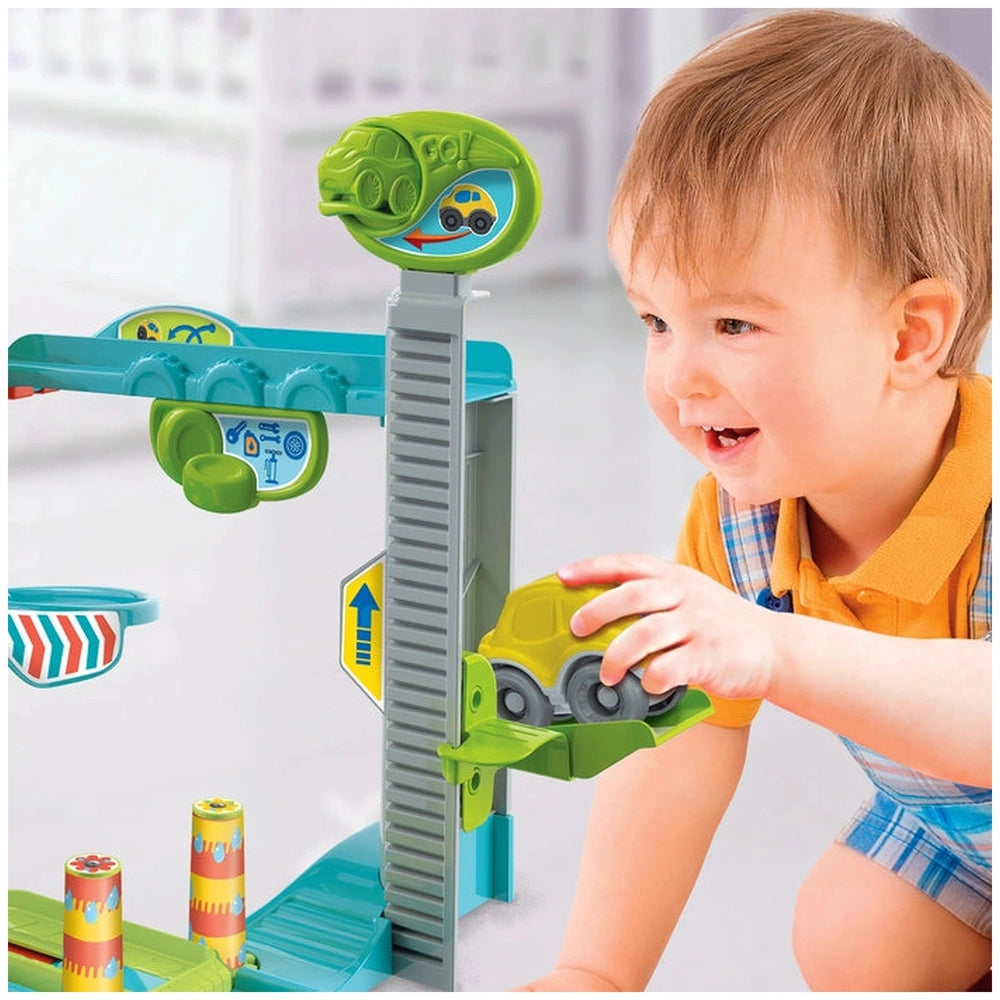 Baby Clementoni Fun Garage activity toy with a young child in a yellow shirt and plaid shorts, smiling and engaging.