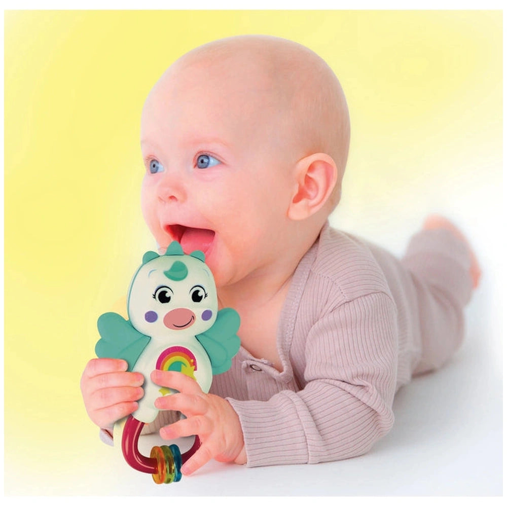 Baby holding a colorful Little Unicorn rattle, lying on a light surface against a bright yellow background.