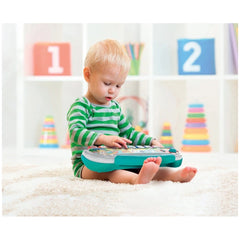 Baby Clementoni Pianola Degli Animali, a young child plays with a green and white toy keyboard on a white carpeted floor.