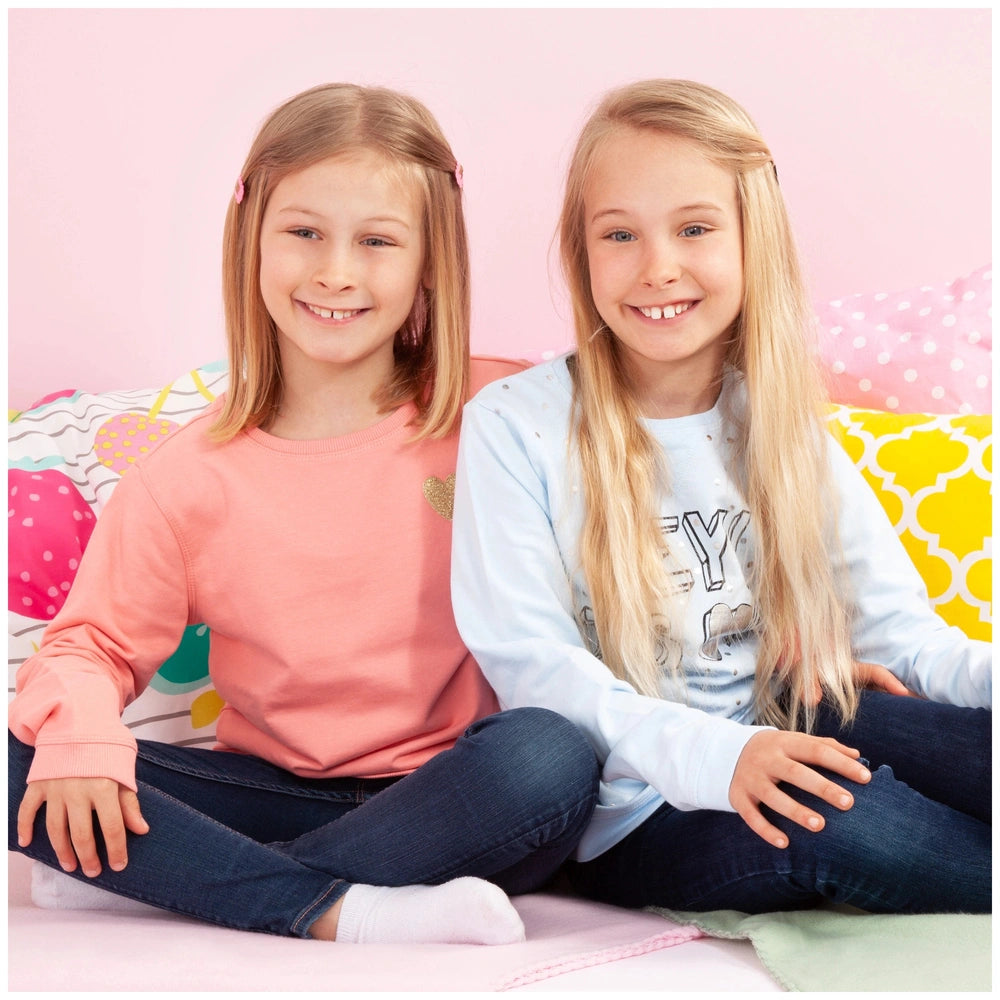 BAYER DESIGN Twin Pram in Unicorn Blue Pink is showcased with two smiling girls on a pink and yellow patterned bed.