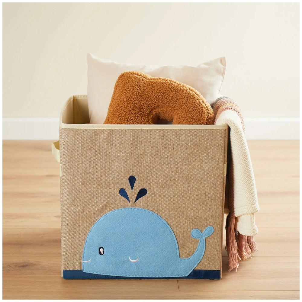 Whale-themed storage box in sand and sky blue, filled with a cozy blanket and decorative pillows, perfect for organizing kids' rooms.