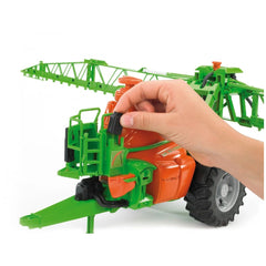 Hand adjusting the green and orange Bruder Amazone UX 5200 Trailed Field Sprayer toy with realistic details.