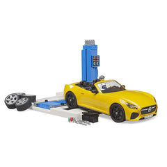 Yellow Bruder Roadster on service lift with tools, extra wheels, and mechanic figure, showcasing car maintenance playset.