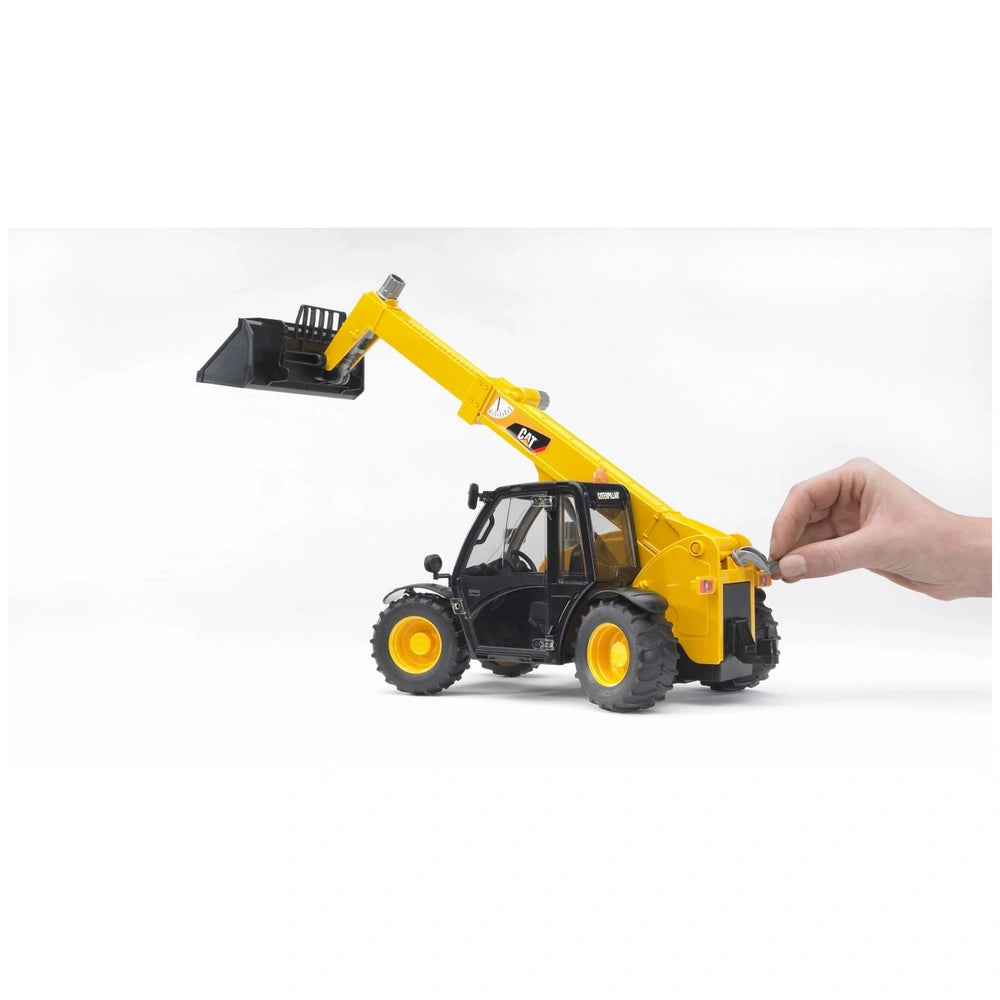 Hand adjusts the arm of a yellow Bruder Caterpillar telehandler toy with realistic details.