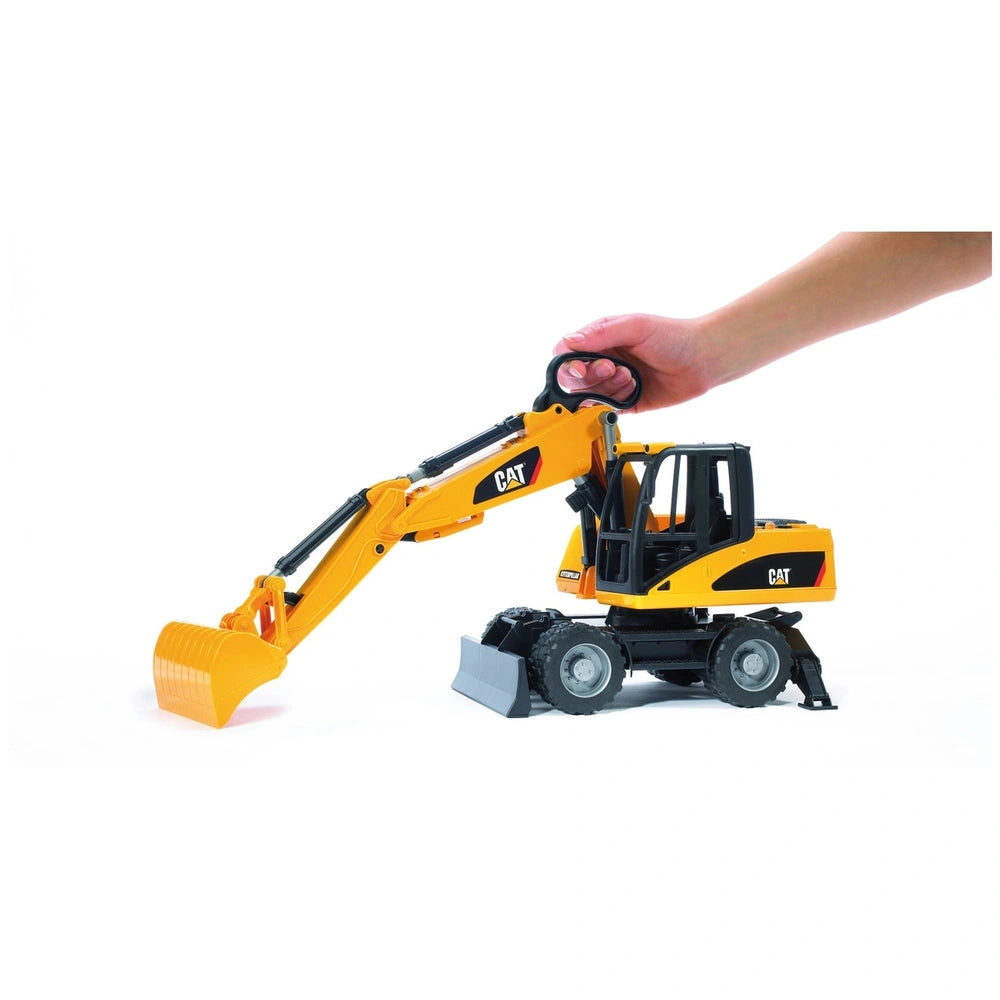 Hand manipulating yellow Bruder CAT Wheel Excavator toy with black wheels and articulated boom on white background.