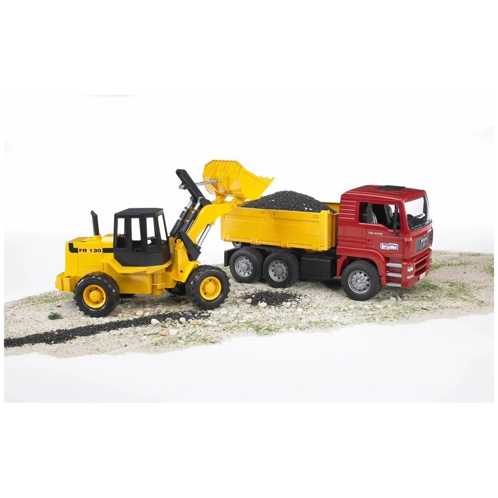 Yellow articulated road loader unloading into red construction truck on sandy terrain.