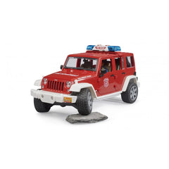 Red Bruder Jeep Wrangler Fire Department toy with detailed design and blue sirens, parked on a small rock.