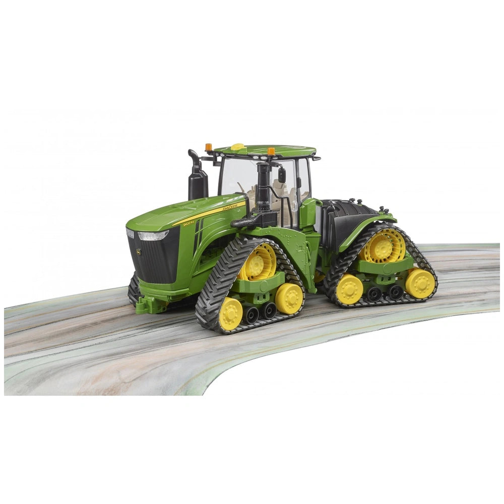 Green Bruder John Deere 9620RX toy tractor with yellow track belts on a curved surface, detailed at 1:16 scale.