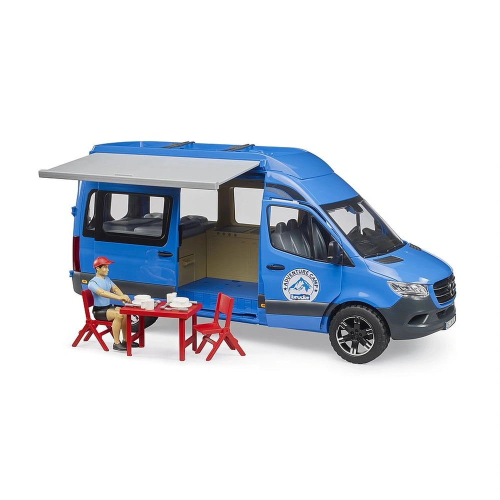 Blue Bruder MB Sprinter camper toy with open doors, retractable awning, and seated driver figure at a red table outdoors.