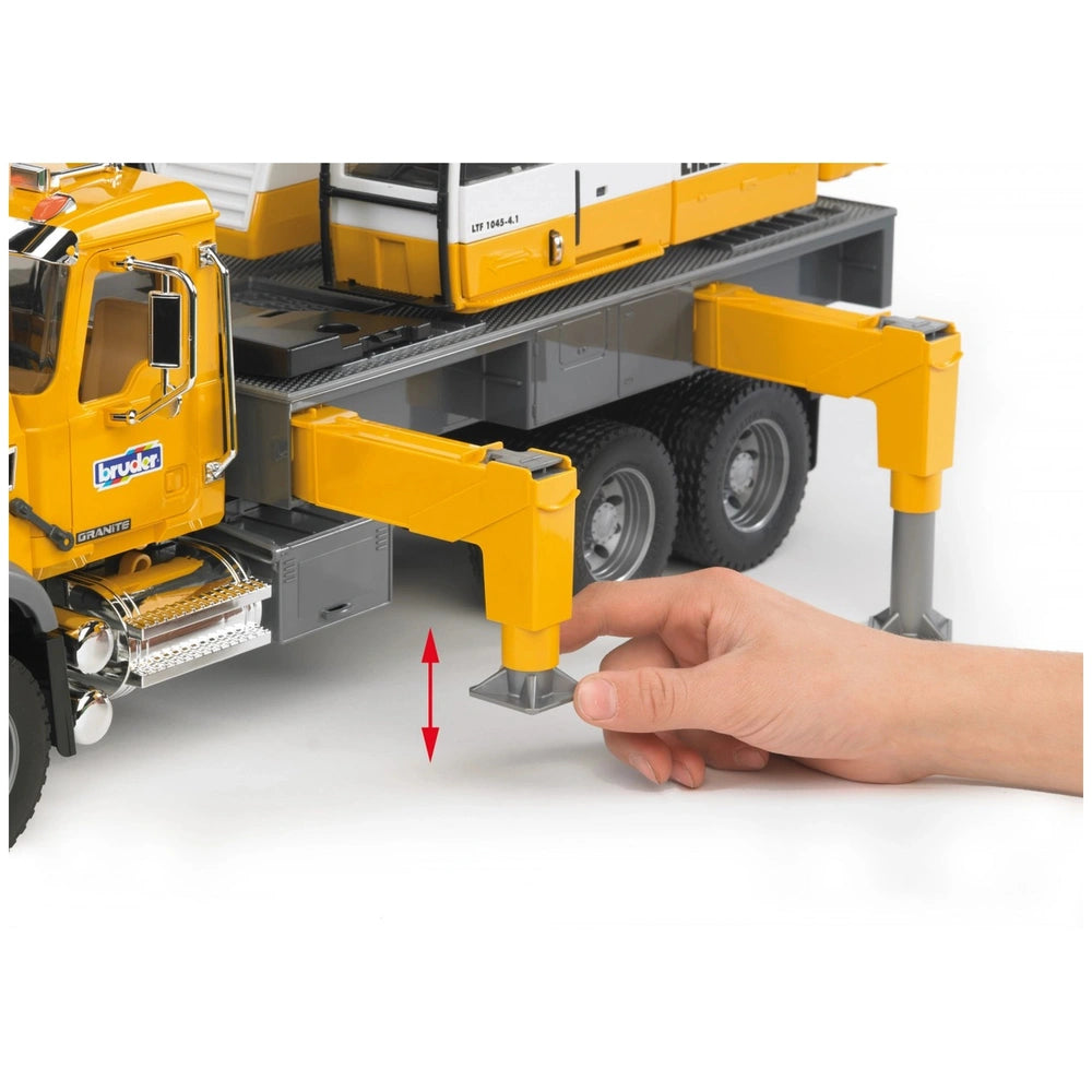 Hand adjusting yellow stabilizing leg of Bruder MACK Granite Liebherr Crane Truck toy with wheels visible.