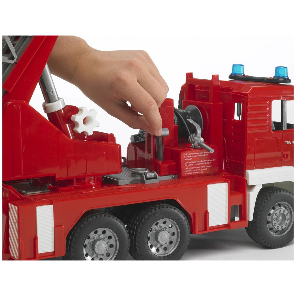 Hand operating the control lever on a Bruder red fire truck toy with a detailed ladder and blue lights.