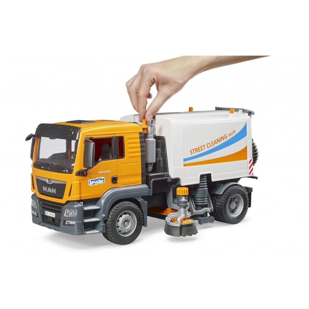 Hand interacting with orange and white Bruder MAN TGS street sweeper toy, featuring detailed cab and street cleaning brushes.