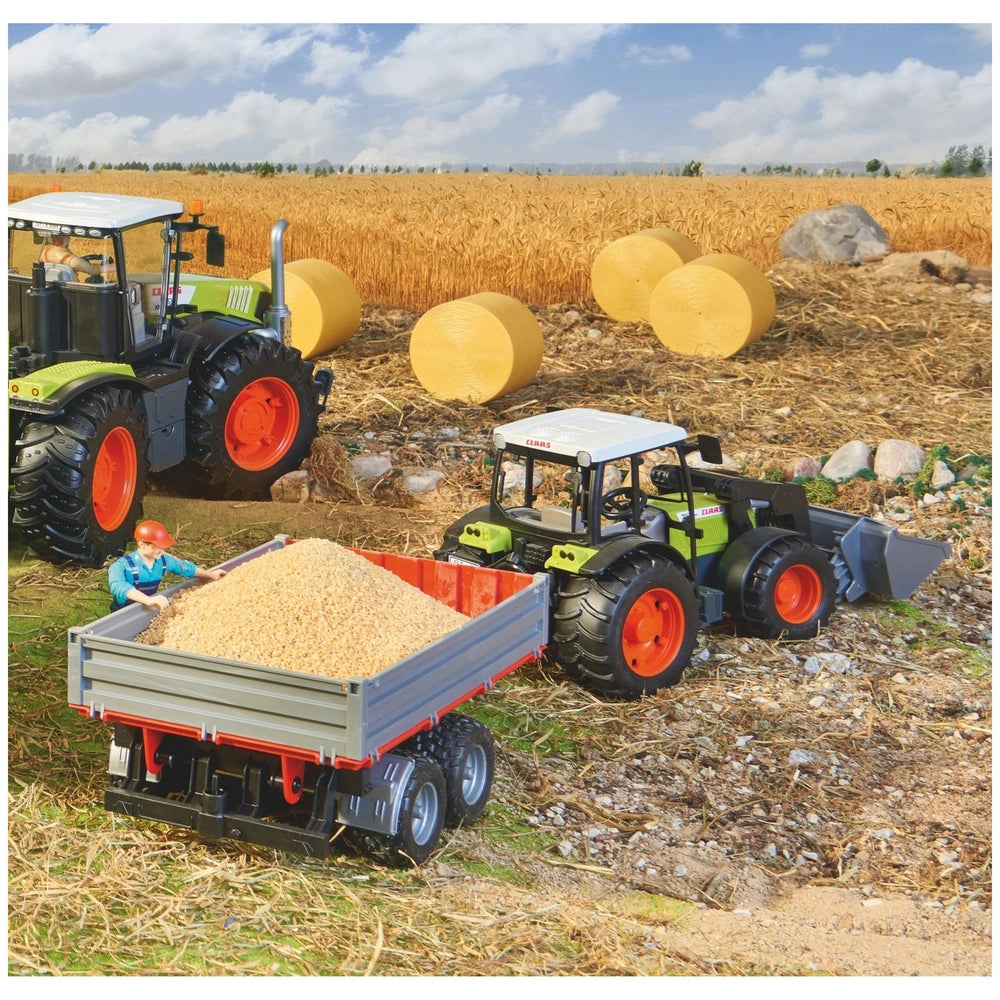Toy tractor and trailer in a wheat field with hay bales and a worker, showcasing BRUDER's realistic agricultural play set.