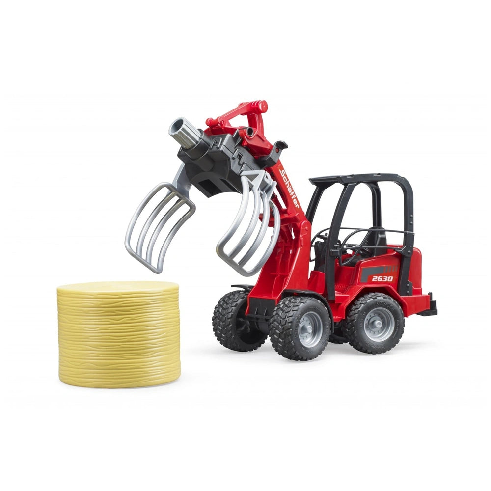 Red Bruder Schäffer Compact Loader 2630 toy with bale gripper holding a yellow bale, featuring realistic details and rugged wheels.