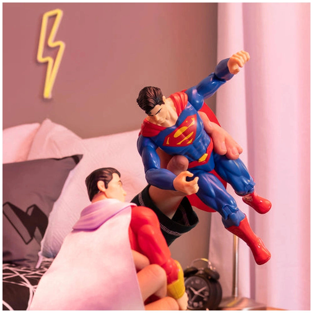 Superman action figure in red costume with flowing cape stands defensively beside Wonder Woman in blue costume on a bed.