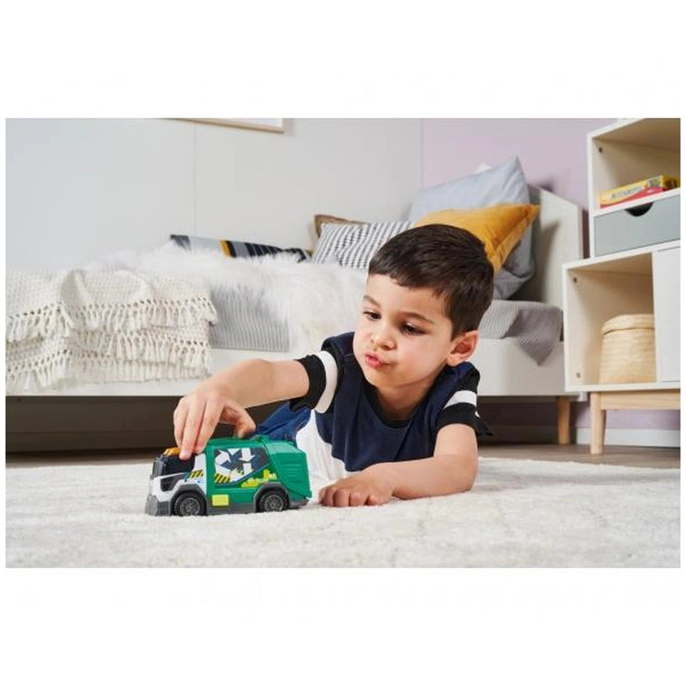 Dickie garbage truck with lights and sounds, green and white toy truck beside a young boy on a light carpet in a cozy living 