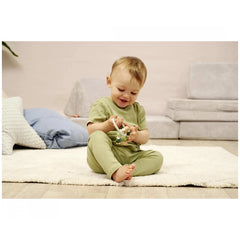 Eichhorn Baby HiPP Grapper with Ring is being held by a smiling child sitting on a light rug in an indoor setting.
