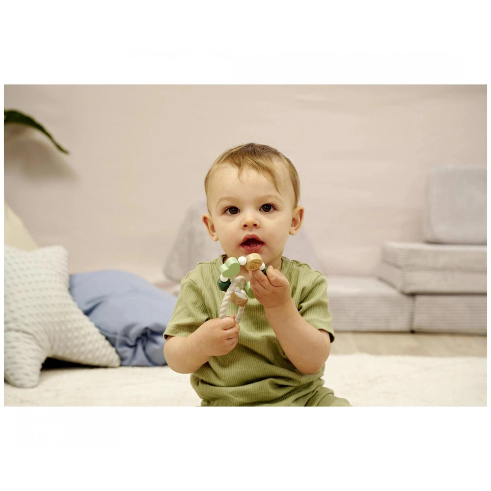 Eichhorn Baby HiPP Grapper is held by a young child in a green shirt, sitting on a carpeted floor surrounded by pillows.