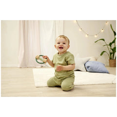Eichhorn Baby HiPP Sound Rattle in a child's hand, surrounded by a cozy indoor setting with a white rug and green decor.
