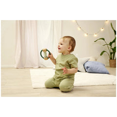 Eichhorn Baby HiPP Sound Rattle is held by a smiling baby on a white rug in a cozy indoor setting with wooden floors.