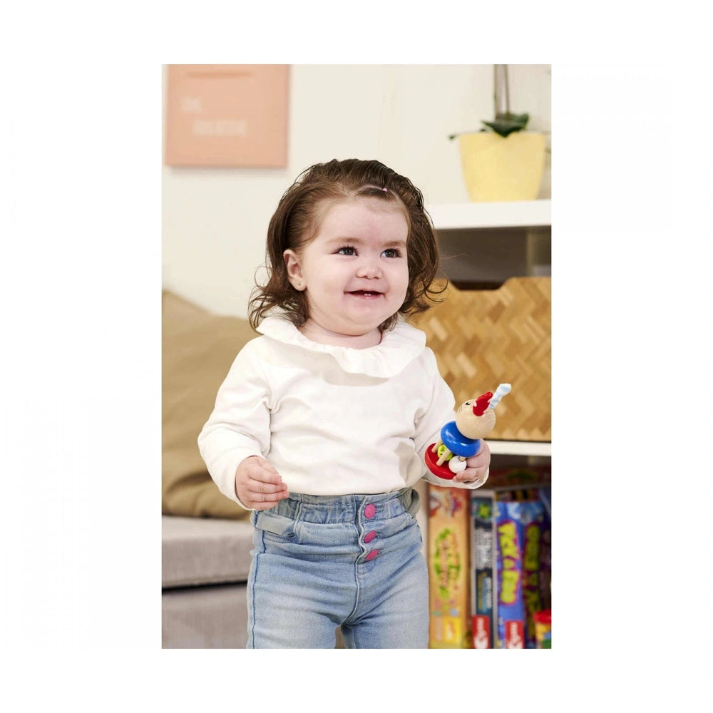 Eichhorn baby wooden rattle rabbit is held by a smiling child in a cozy indoor setting with wooden furniture and a plant.