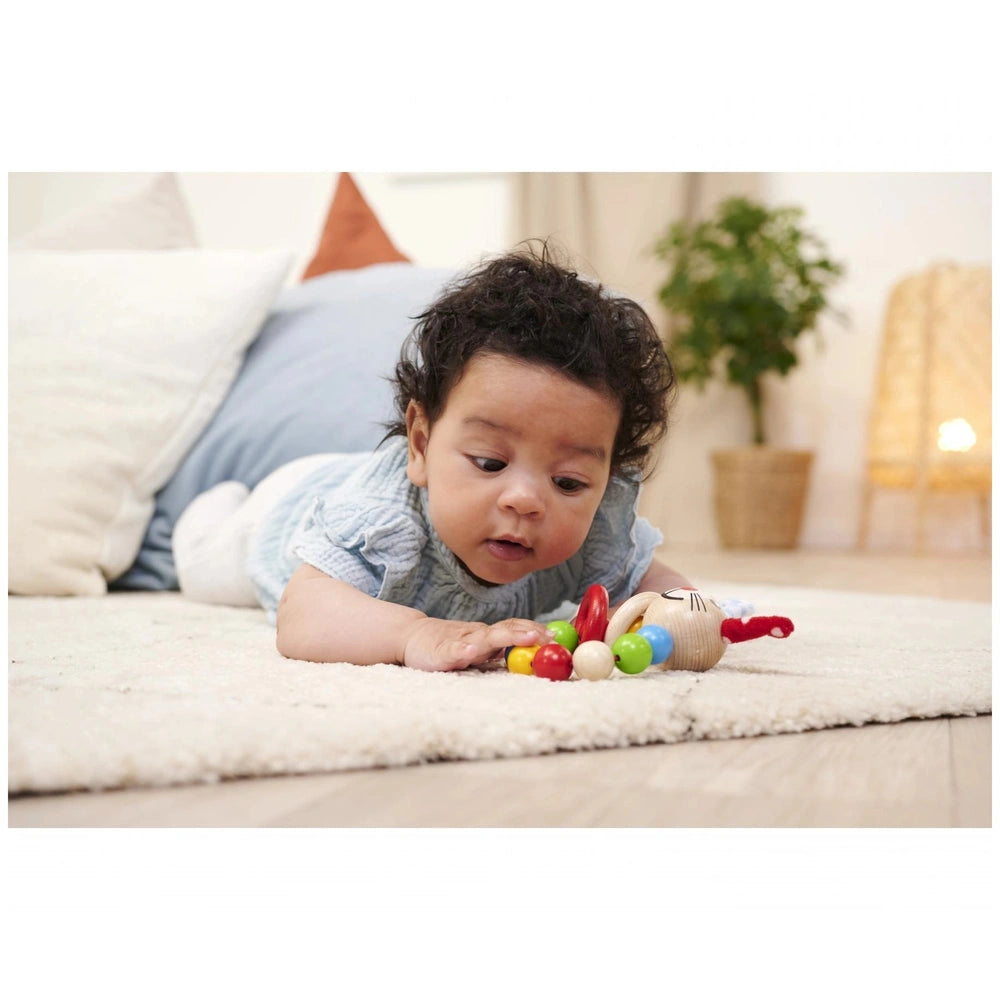 Eichhorn baby wooden teething ring rabbit lies beside a young child in a light blue outfit, engaging with a colorful toy on a