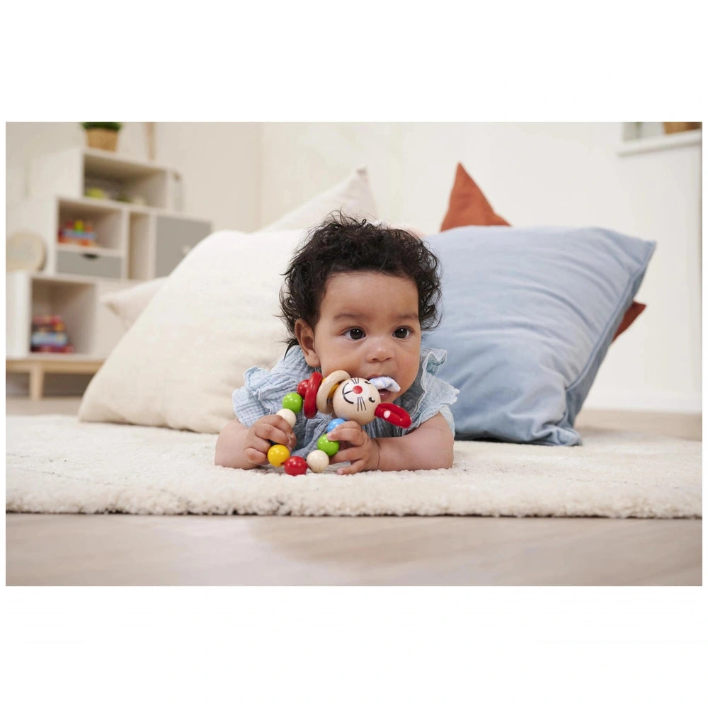 Eichhorn baby wooden teething ring rabbit placed in a cozy nursery scene with a baby on a white rug and a stuffed animal.
