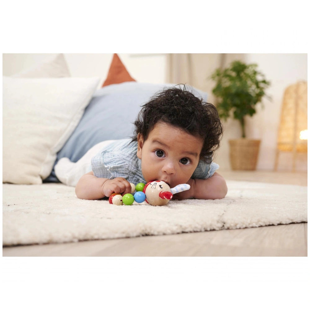 Eichhorn baby wooden teething ring rabbit held by a child lying on a soft, light-colored rug with a neutral expression.
