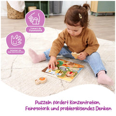 A child in a brown sweater and blue jeans sits on a white rug, intently reading a colorful children's book.