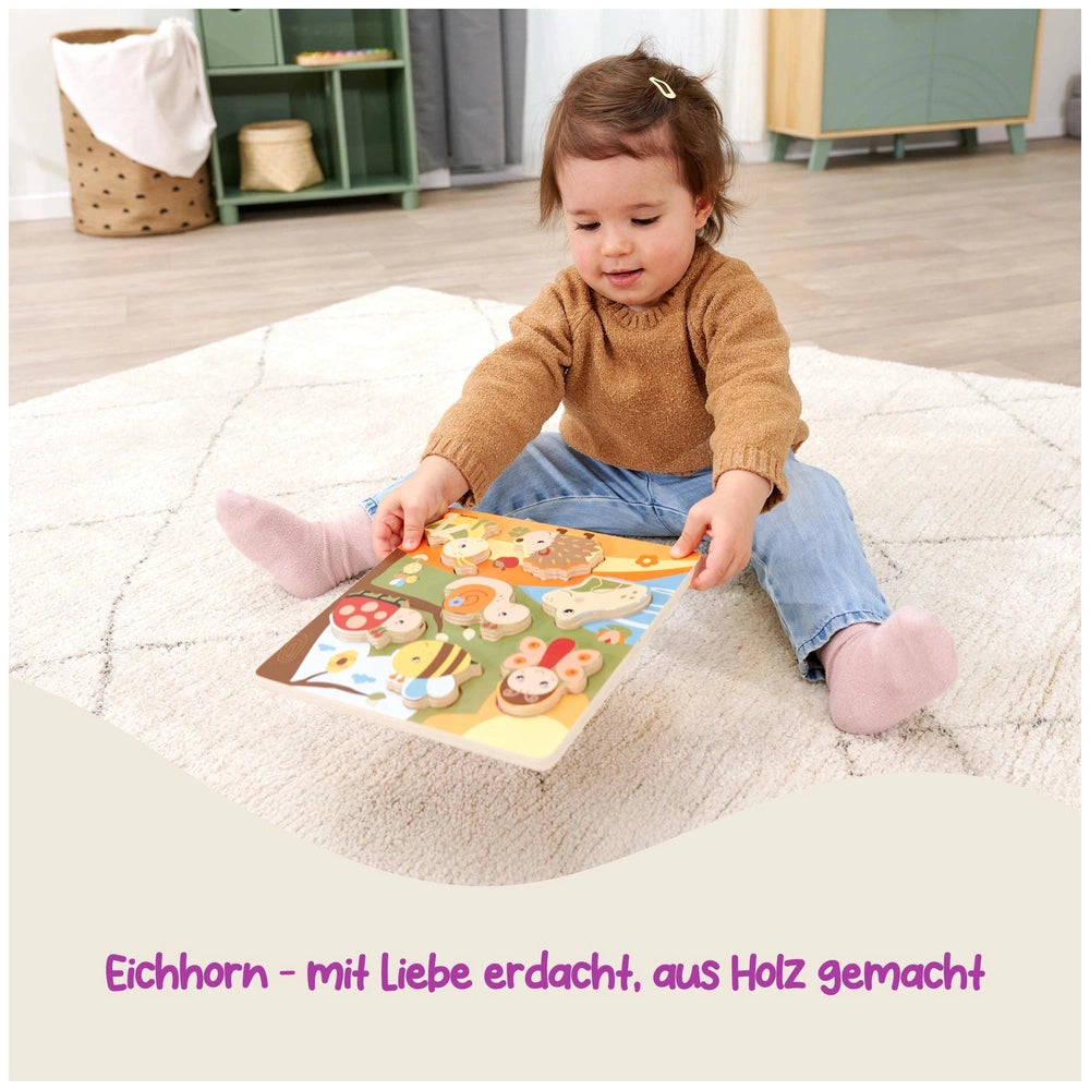 Eichhorn Bee-Happy Sensory Puzzle is surrounded by a young child reading a colorful book on a light shaggy rug.