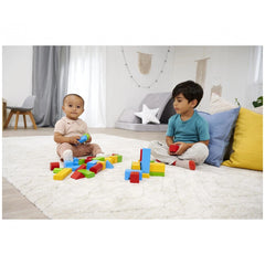 Eichhorn coloured wooden blocks are scattered on light carpet as two children play with plastic toys in a bright, minimal liv