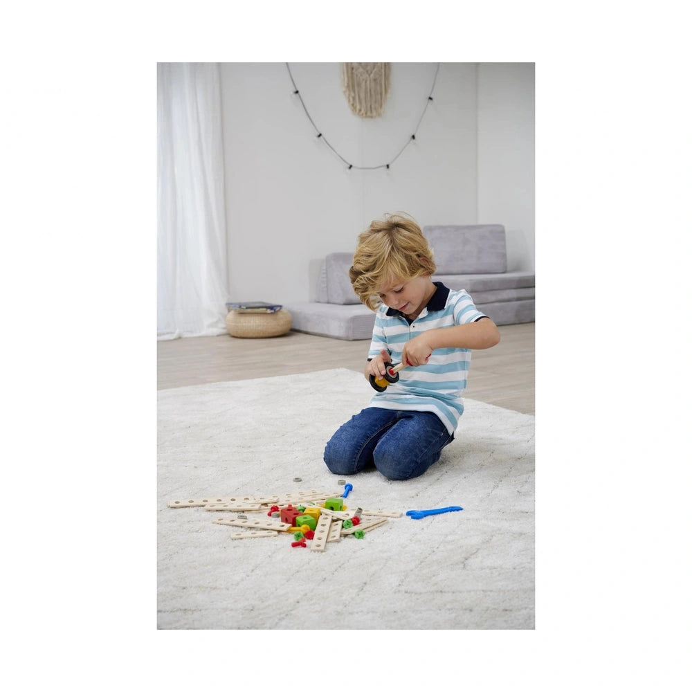 Young child in a blue and white striped shirt holds a yellow screwdriver, surrounded by colorful wooden blocks and toys.