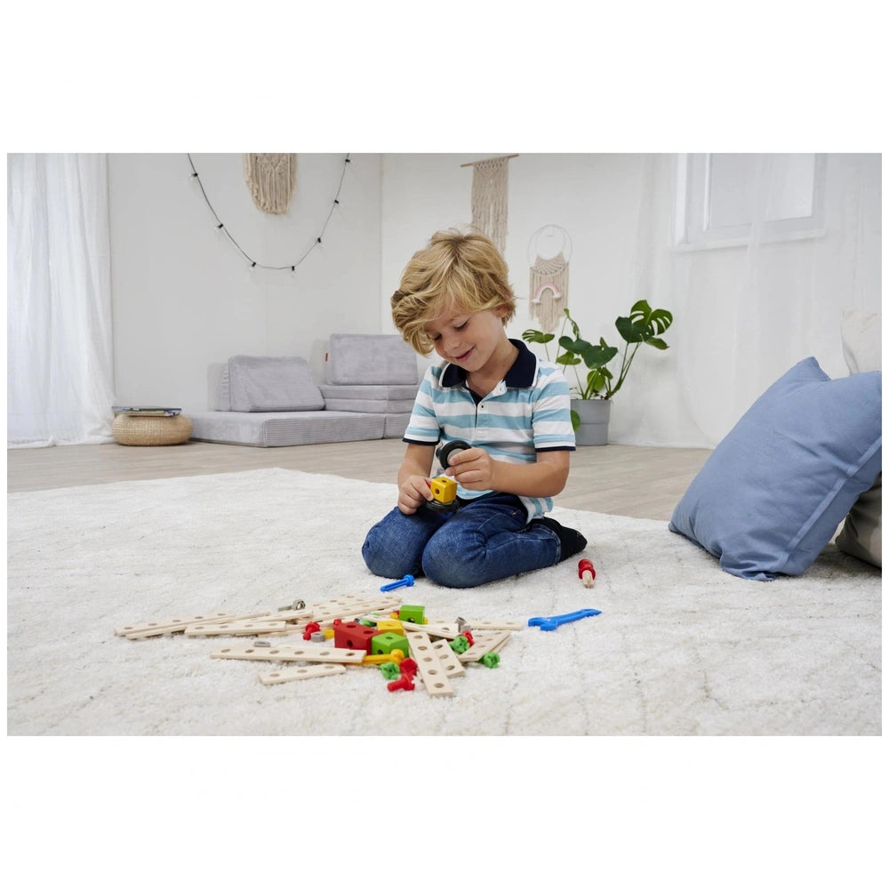 Eichhorn Constructor Expansion Set with wooden toy components, a child playing on wooden flooring with a blue pillow and gree