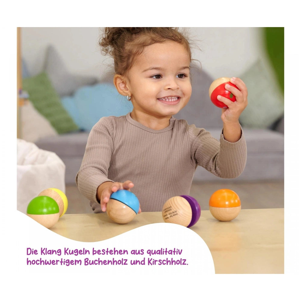 Eichhorn Wooden Music Balls set with a joyful child holding a red ball, surrounded by colorful wooden balls on a table.