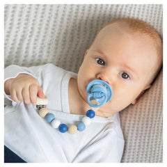 GOKI Soother Chain Star baby activity toy held by a blonde baby in a white shirt on a white and gray patterned surface.