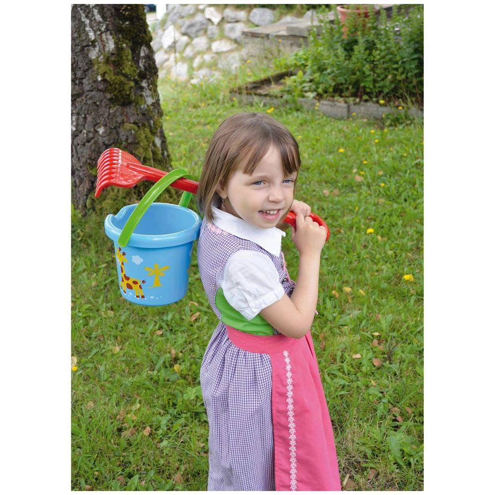 Gowi beach bucket in blue with yellow handle and red spout held by a girl in a pink checkered dress outdoors.