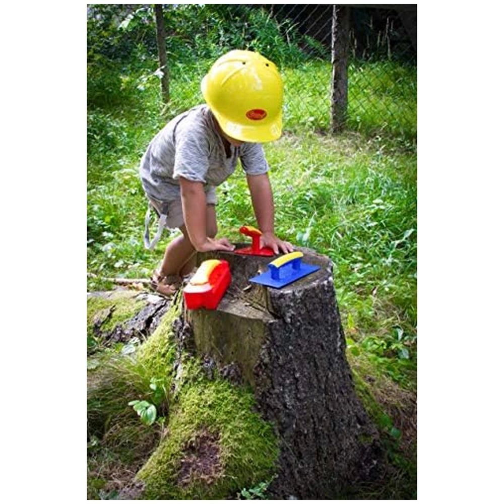 Gowi Design Bricklaying Set features a person in a yellow hard hat holding a red and yellow tool on a mossy stump.