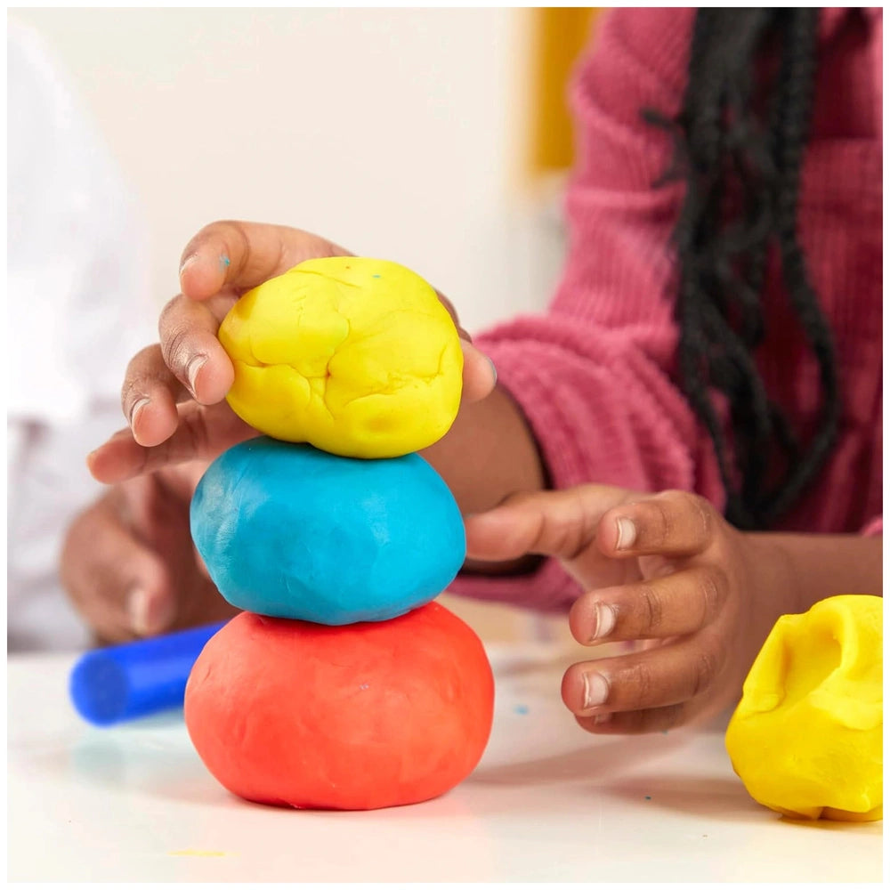 Play-Doh 15 Cans Party Bag featuring stacked red, blue, and yellow clay balls on a table with additional colorful objects.