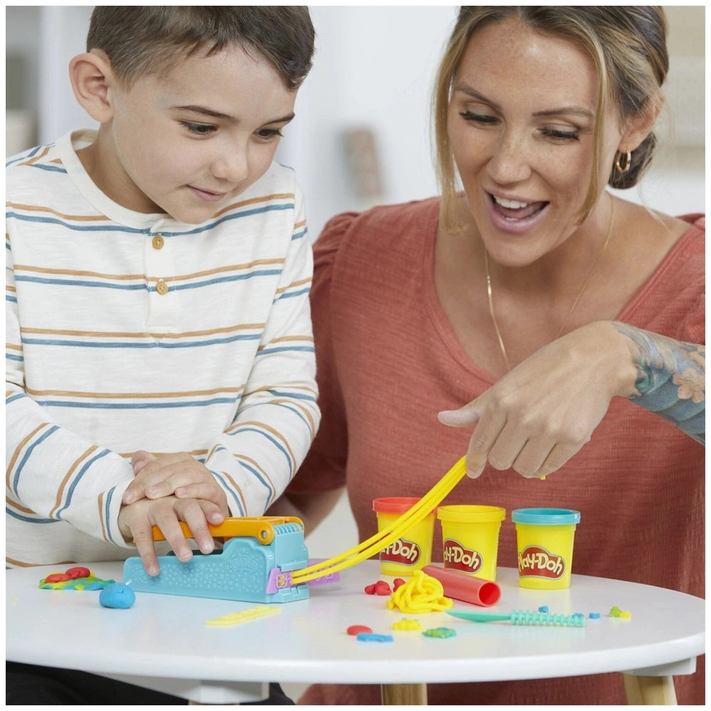 Hasbro Play-Doh Fun Factory Starter Set displayed on a white table with a woman in red and a child in striped top, engaged in