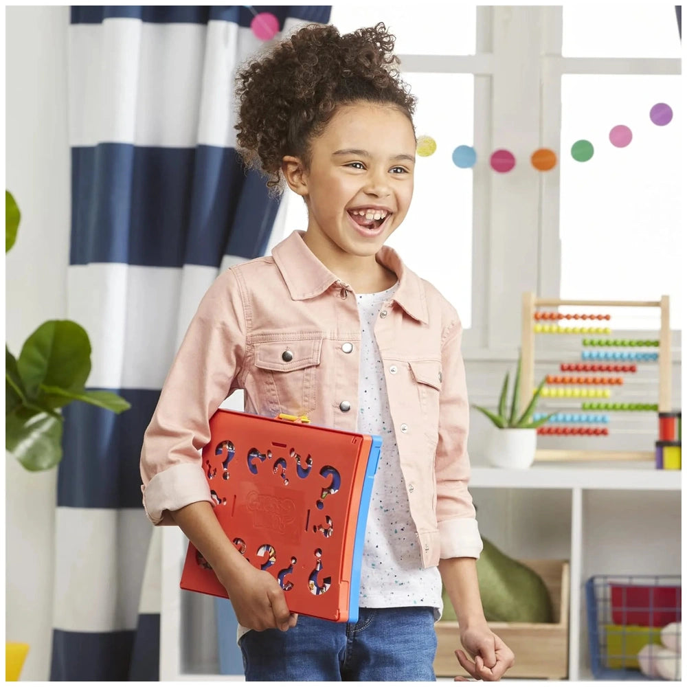 Hasbro Wer Ist Es board game in a lifestyle scene with a girl in a pink jacket holding a colorful book.