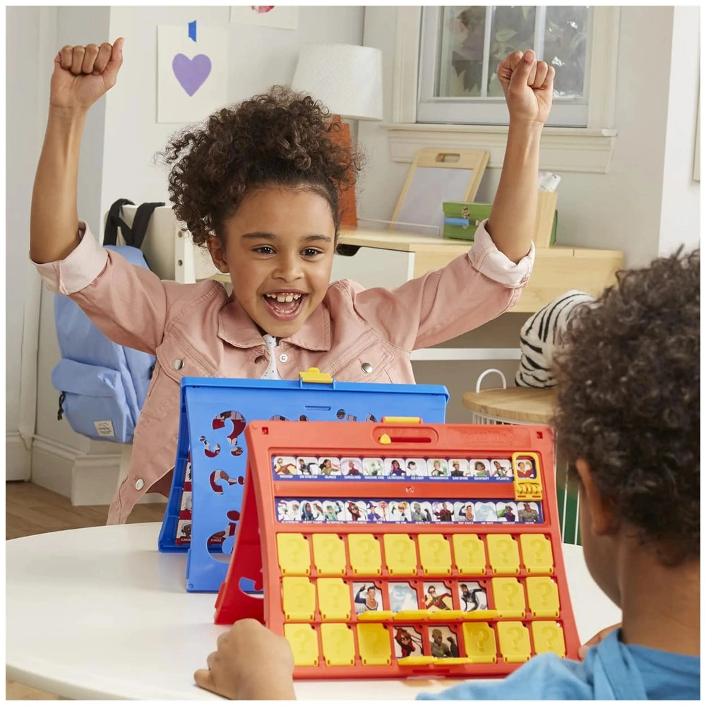Child playing Hasbro Wer Ist Es Board Game on a white table, wearing a pink jacket and shirt, with curly dark hair.